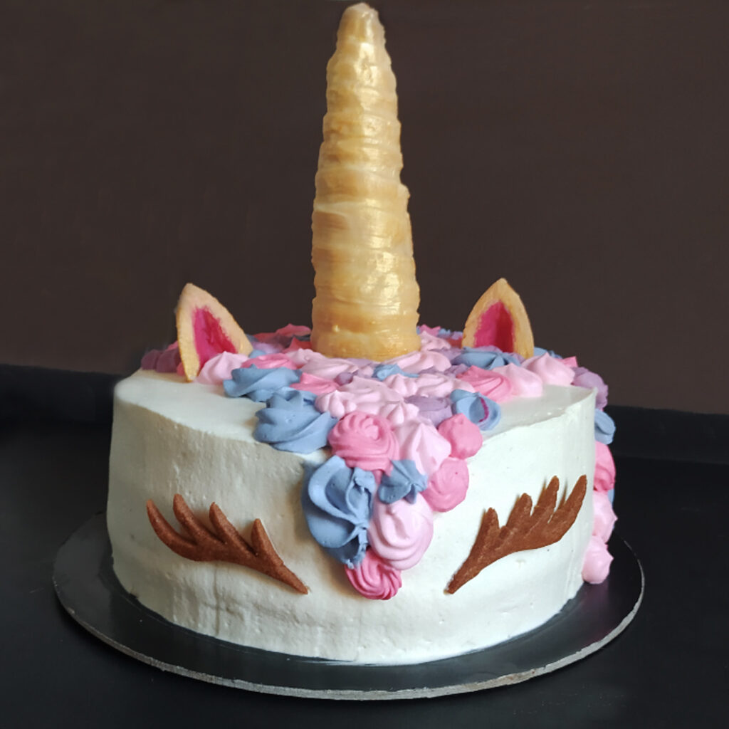 torta chantilly con corno, orecchie e occhietti in biscotto e panna in diverse tonalità di rosa e lilla in superficie